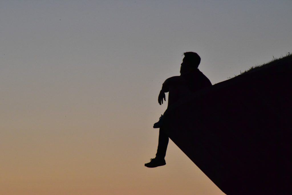 A photo of a man's silhouette on a cliff thinking about life.