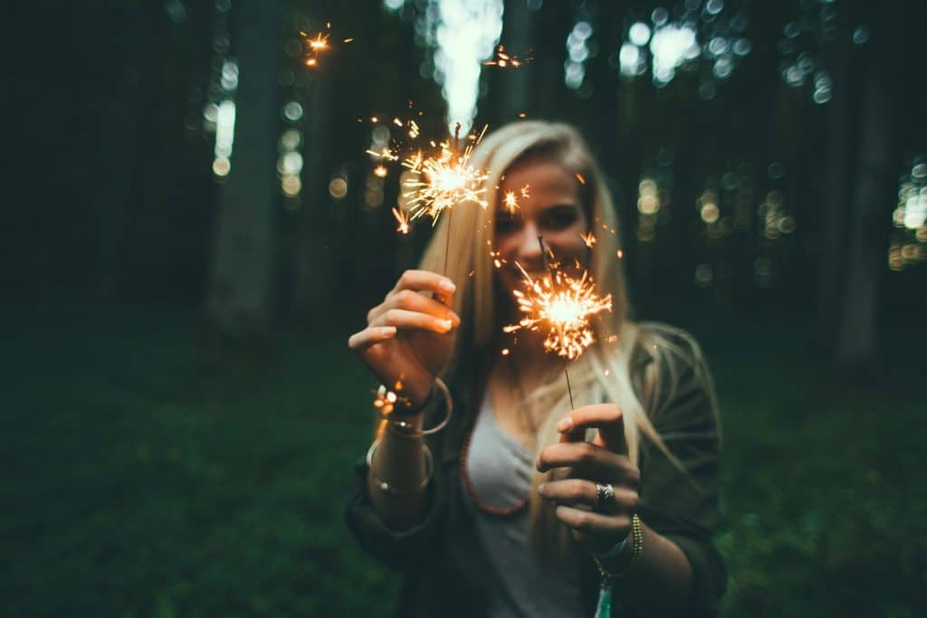 Picture of a woman smiling with sparklers in her hands finding happiness in nature.