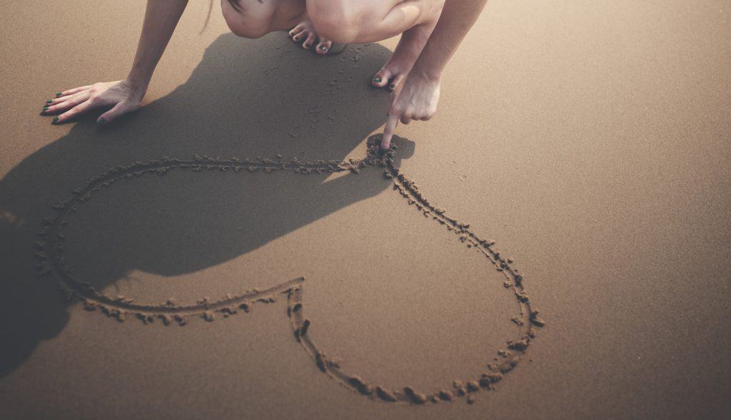 An image of a girl drawing a heart in the sand.