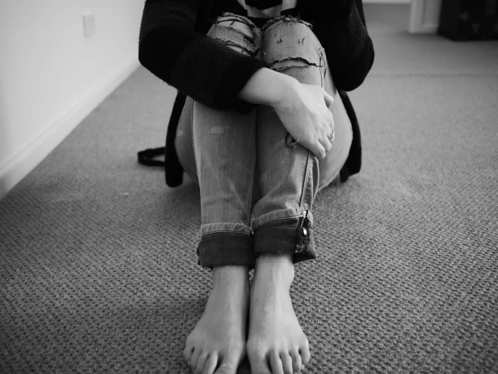A black and white photo of a woman hugging her knees when she's not ok.