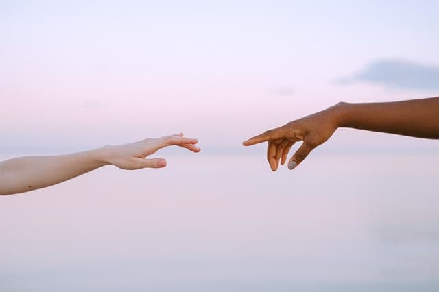 An image of an African American and Caucasian hand reaching out to one another.